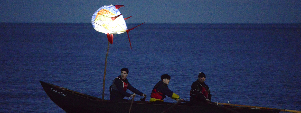 Photo of boat with men rowing using a large fish shaped lantern