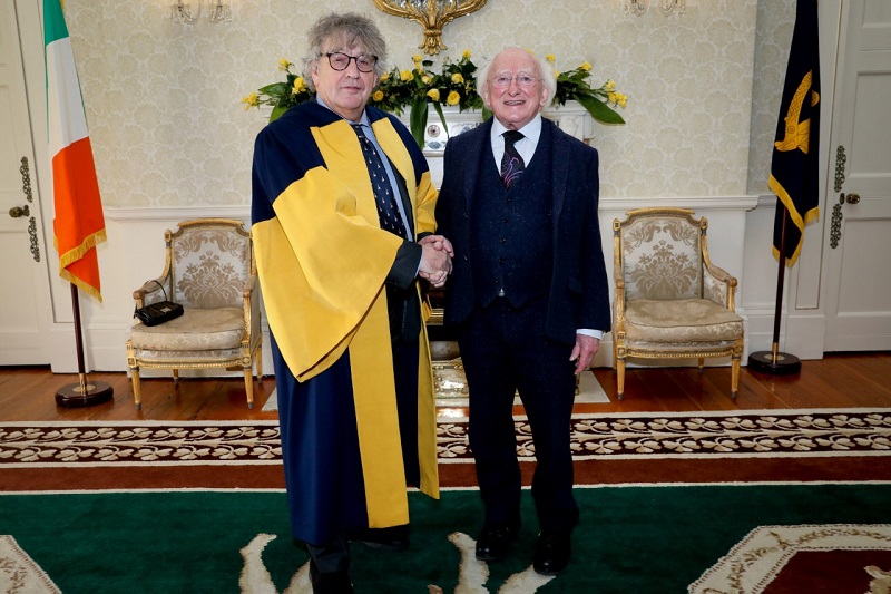 President Higgins and Professor Paul Muldoon smile as they shake hands at Áras an Uachtaráin